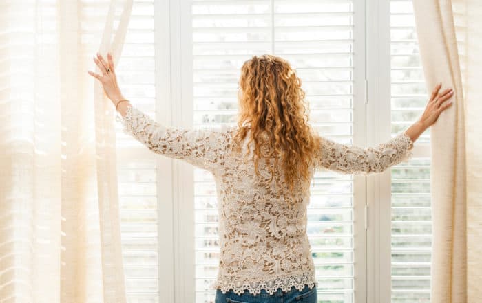 Woman parting curtains to look out window