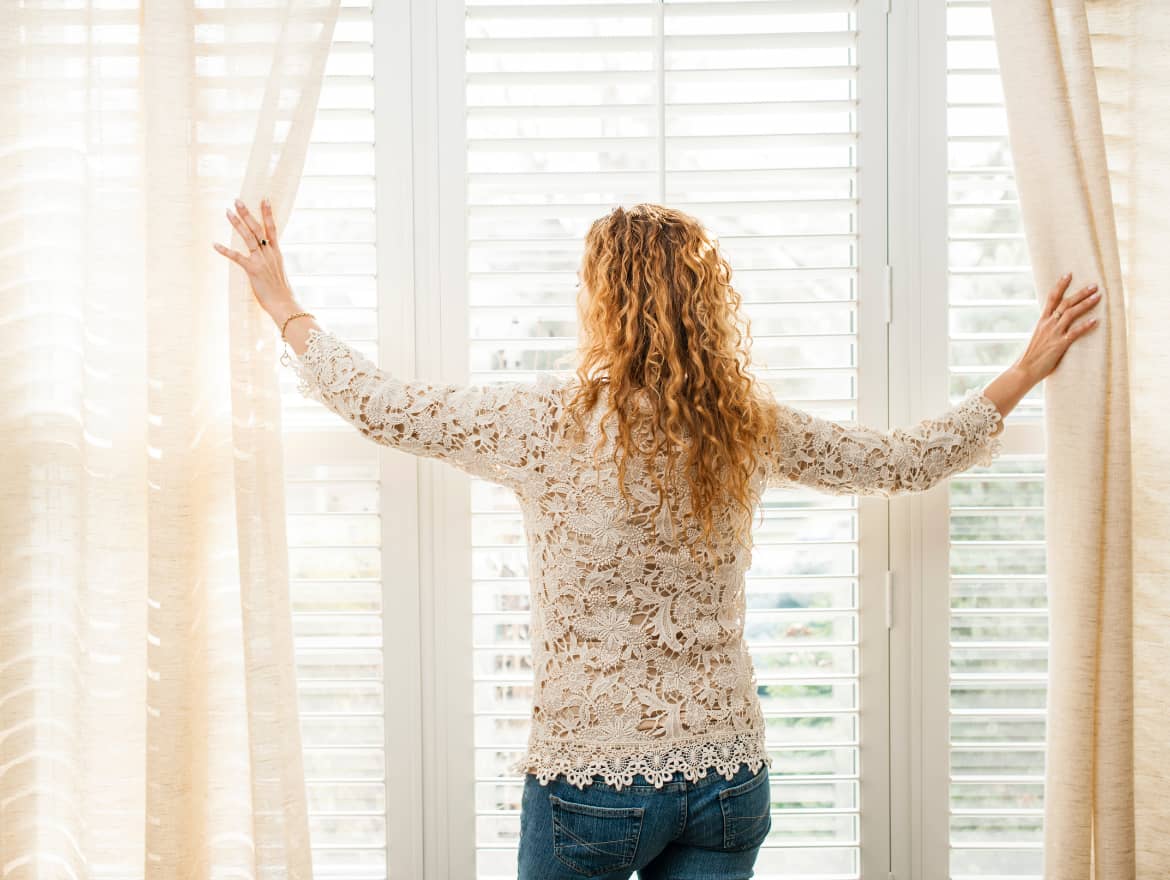Woman parting curtains to look out window